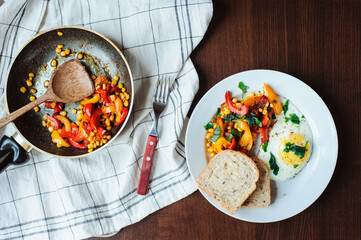 tasty vegetarian farm style breakfast - fried egg with baked sweet peppers and corn with parsley and whole grain bread served on white plate