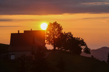 Naklejka na ściany i meble Sonnenaufgang hinter Bauernhof mit Baum färbt den Himmel Orange
