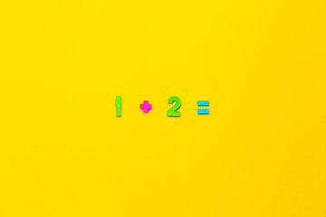 Mathematical example one plus two is equal on yellow background made of children's plastic numbers....