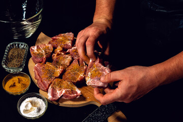 Marinating pork neck skewers, adding salt, curry and basil to the meat, pieces of meat on a wooden board.