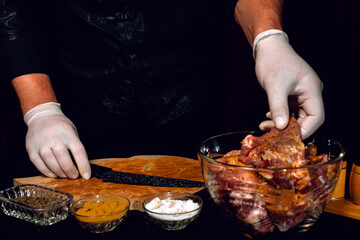 The chef in white gloves rubs pieces of pork with spices, uses curry, basil and salt, marinates the meat on a barbecue.