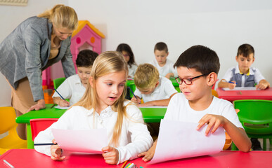 Fototapeta na wymiar Portrait of two schoolkids and their teacher helping children in classroom