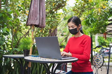Young woman working with laptop and wearing black face mask at coffee shop, New Normal and smart...