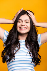 brunette long haired woman with curls touching head and smiling isolated on yellow