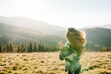 Young tourist girl on top of enjoying sunset. Back view. Woman walk in the autumn grass in mountains on vacation. Holiday trip concept. World Tourism Day.