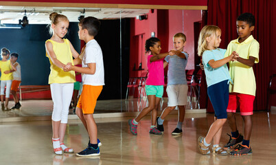 Group of glad positive smiling childrens trying dancing with partner in classroom