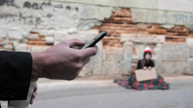 A homeless girl looks at a businessman who uses his phone to send e-mail.