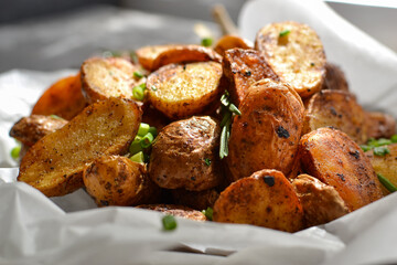 rustic potatoes. Baked potatoes with green onions and herbs on a plate with parchment. Gray background. Close-up. light from the window.