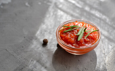 Ketchup in a glass bowl. Gray background. Tomato sauce with rosemary. Free space for text.