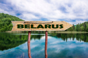 Belarus wooden arrow road sign against lake in the forest. Travel to Belarus concept.
