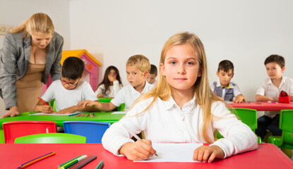 Portrait of little girl with pen and notebook at lesson in elementary school