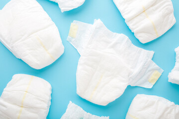 Many white baby diapers on light blue table background. Pastel color. Top down view. Closeup.