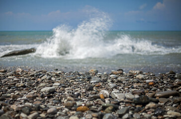 Wet pebble stones on the sea beach against a blurred background of storm waves and blue sky.