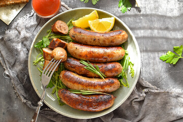 Grilled sausages with lemon and ketchup. Bavarian sausages with herbs and rosemary. Gray dark background. Gray plate and linen napkin. Free space for text