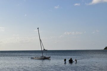 Beautiful picture of a man fishing in a bay close to a sailing boat. Relaxing environment.