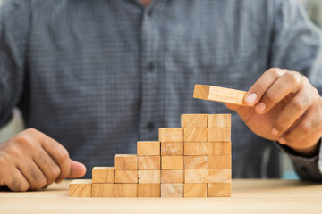 Close up male hand holding arranging or pick up the block wood game and stacking. Growth of Business financial investment and bankrupt concept.