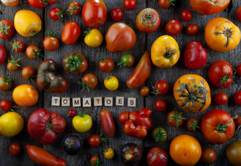 Tomatoes of different varieties and colors top view. the word Tomatoes is inscribed in wooden letters. Layout on a wooden background. Food.