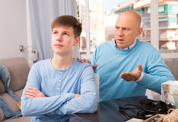 Obraz premium Portrait of son ignoring irritated father sitting in home interior