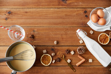 cooking, culinary and christmas drinks concept - pot with eggnog, ingredients and aromatic spices on wooden background