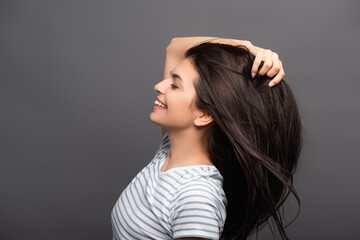 side view of brunette woman with closed eyes smiling and touching hair isolated on black
