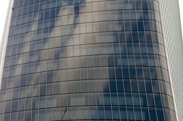 Fototapeta na wymiar skyscraper in the city: detail of the windows with self-supporting glazing and modules with linear elements. On the glass reflections of the sky and clouds.
