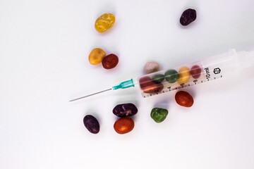 On a white background, a medical syringe is filled with colorful candies. The concept of necessity in diabetes