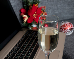 A glass of champagne and a laptop against the background of festive red Christmas decorations. the concept of celebrating in the office of Christmas or New Year. selective focus.