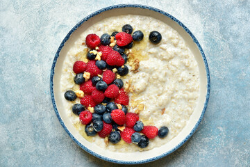 Oatmeal porridge with fresh berries and honey for a breakfast, Top view with copy space.