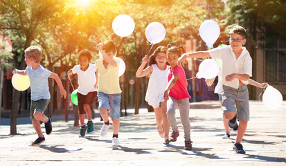 Group of happy kids with balloons running in race in the street and laughing outdoors