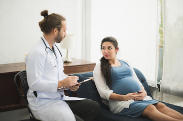 A doctor examining the pregnancy woman sitting on sofa near window.