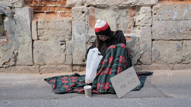 Homeless girl sitting on the street and opens a package of food.