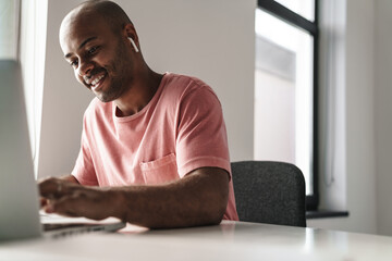 Image of smiling african american guy working with laptop