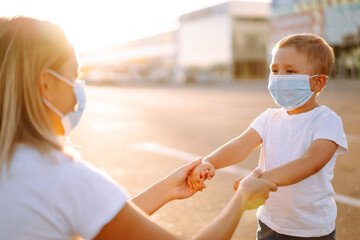 Little boy and mom in medical mask in quarantine city at sunset. Virus and illness protection. Covid-2019. Kids safety. 