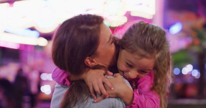 Authentic shot of a happy excited little girl is having fun and smiling in camera in amusement park with luna park lights at night.
