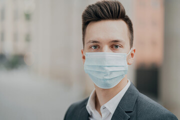 portrait of a business man businessman, looking at the camera through a protective mask from coronovirus. thinking about a business meeting in the future. background the city