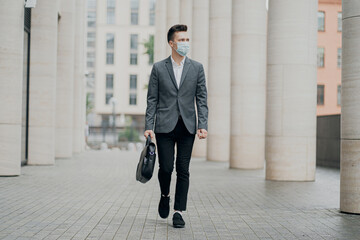 a stylish business man in a gray suit walks through the business center, wearing a face mask that protects against pandemics, coronaviruses, viruses, and allergies. 