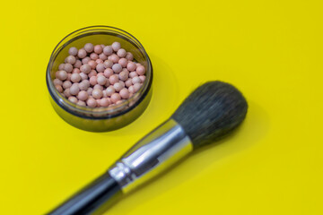 Cosmetic powder balls blush and makeup brush close-up, shallow depth of field. Bright yellow background. Brush is out of focus