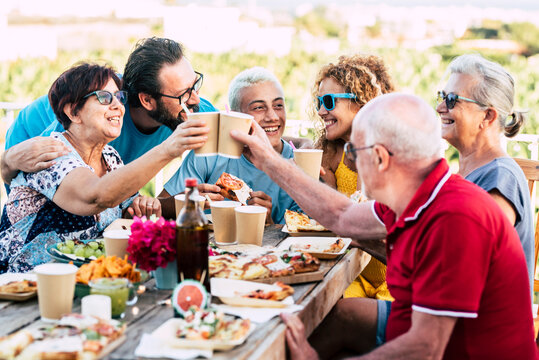 Group of different ages people celebrate and eat together in friendship outdoor at home - happy young, adult and senior have fun clinking and enjoying food on a wooden table - celebration 