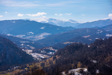 mountainous countryside in early spring. dry grass and leafless trees on the hillside. snow in the distant valley and ridge