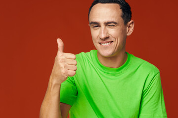 A man in a green T-shirt on a red background winks at the camera 