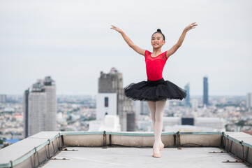 Fototapeta na wymiar Asian ballerina girl dancing on the rooftop of the building city background.