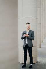 a male businessman holds a new phone in his hands and writes a message to his partner at work. Grey business suit, brunette hair stylish barbershop hair salon.