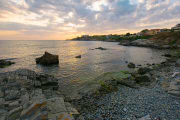 sunset at the coast of black sea. wonderful dramatic landscape with rocks on the pebble beach beneath a cloudy sky. velvet season vacations