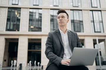 business man a man of European appearance, working on a laptop new projects creating buildings. stylish haircut, glasses, gray business suit from a fashion store.