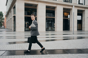 business man goes to work in the office a man of European appearance, stylish haircut, glasses, gray business suit from a fashion store. he holds a laptop with projects in his hands