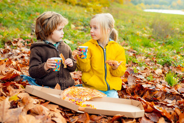Kids eating pizza on falling autumn maple leaves background. Children, childhood lifestyle concept.
