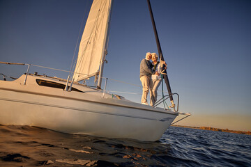 Full length of a romantic retired couple, senior man and woman standing on the side of sail boat or...