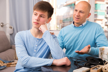 Portrait of father calming upset teenage son after quarrel