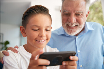 Hispanic Grandson Showing Grandfather How To Use Mobile Phone At Home