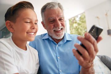 Hispanic Grandson Showing Grandfather How To Use Mobile Phone At Home